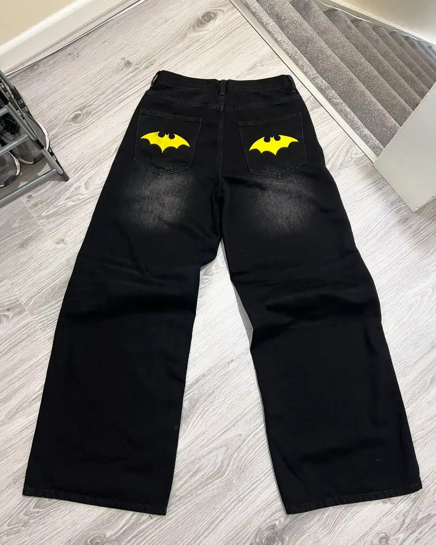 "Black denim jeans featuring detailed retro Batman logo embroidery on the back pocket, offering a sleek, modern fit with a bold superhero-inspired design."